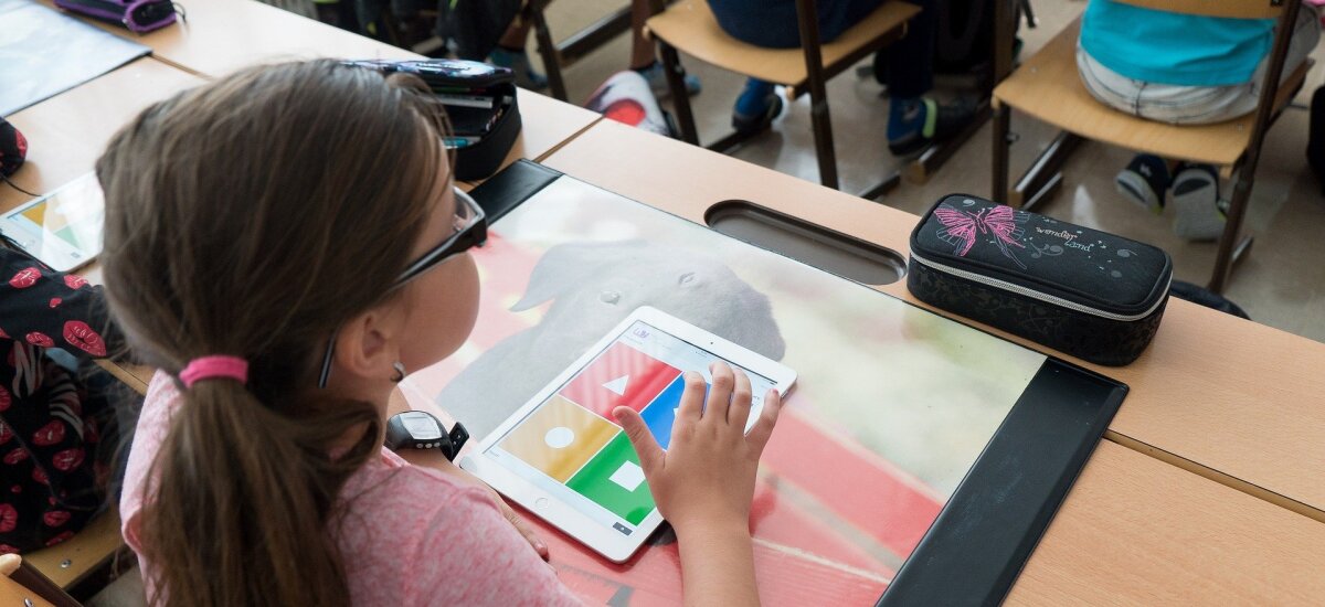 Das Bild zeigt ein Schulkind an seinem Tisch mit einem Tablet